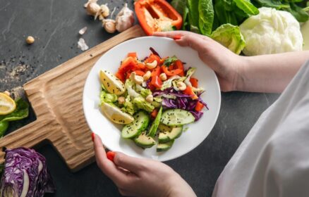 Fresh vegetable salad in female hands against the background of a dark tabletop.
